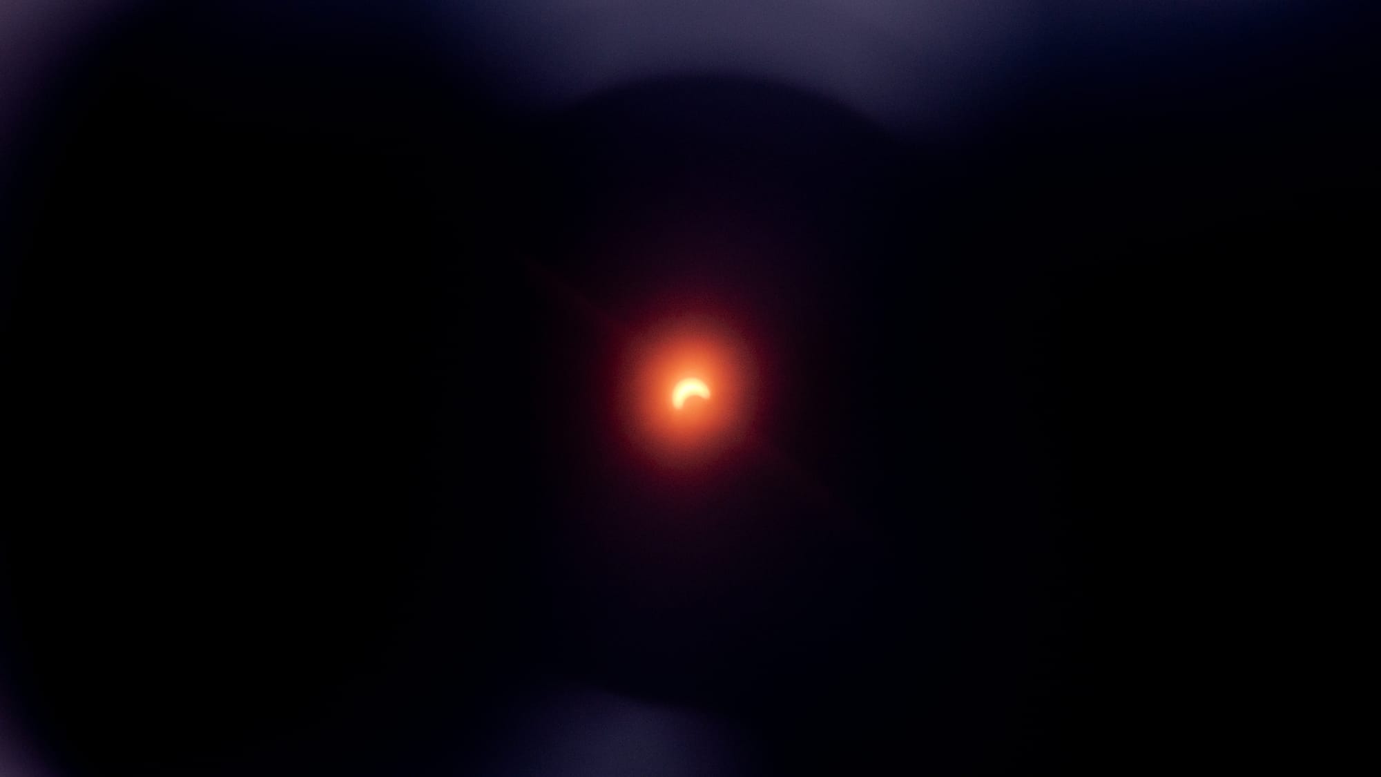The 2024 solar eclipse, photographed in the Chicago area. About half of the sun is obscured by the moon as an orange glow emanates against the dark backdrop.