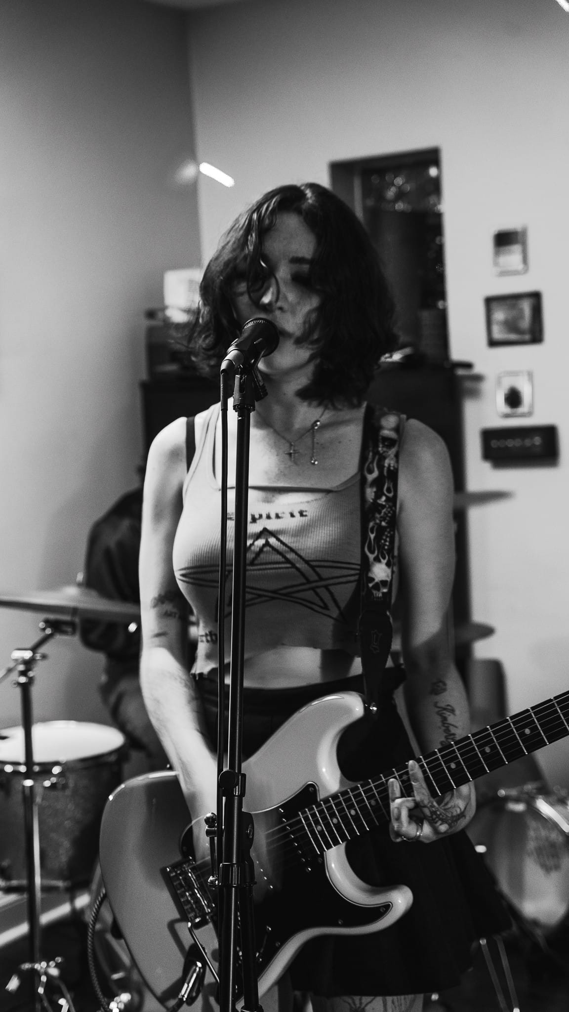 A black-and-white photo of a woman playing an electric guitar while singing into a microphone.